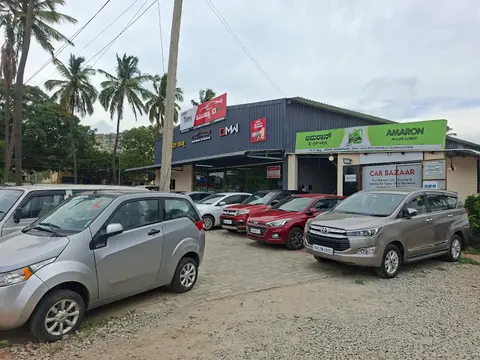 Cars parked close together on the gravel forecourt: a silver hatchback, a red compact, an Innova and others.